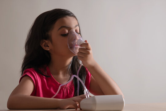 Young girl sitting and inhaling through a nebuliser at home. (Children) 