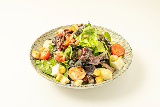 Mixed greens salad with cubed cheese, croutons, cherry tomatoes, pomegranate seeds, and olives in speckled bowl
