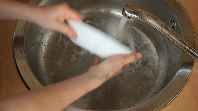 Doing dishes routine, rinsing soapy bowl under running water stream