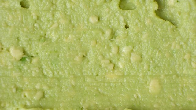 Close-up of a knife scraping fresh green guacamole texture to create copy space.