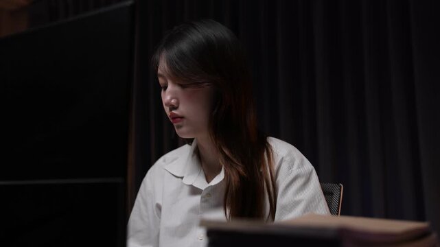 Asian businesswoman working late on a computer in a dark office.