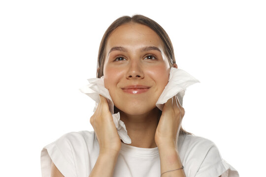 Portrait of a young smiling woman wiping her face with wet wipes, skincare routine, on white background