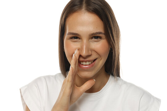 Portrait of a laughing young woman whispering a secret with hand near mouth, natural beauty, on white background.
