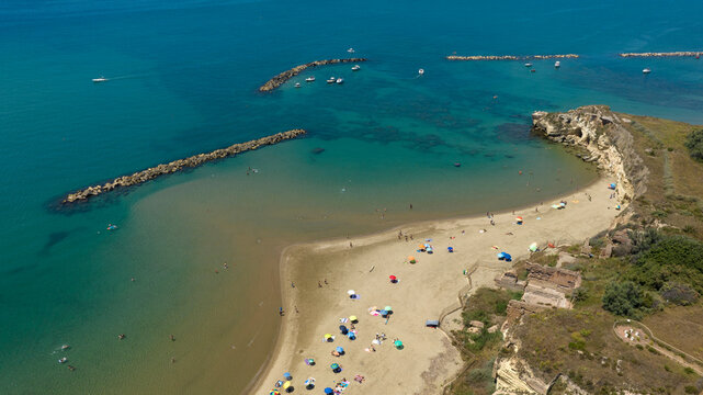 Aerial view of Grotte di Nerone Beach in Anzio, Italy, showing the sandy cove with beach umbrellas, adjacent to ancient Roman ruins and sea caves, and protected by breakwaters in the Tyrrhenian Sea.