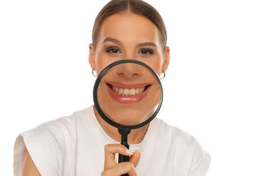Portrait of smiling woman holding magnifying glass over teeth, dental care concept, on white background