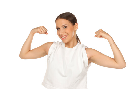 Front view portrait of a confident young woman flexing arm muscles, smiling with teeth, on white background.