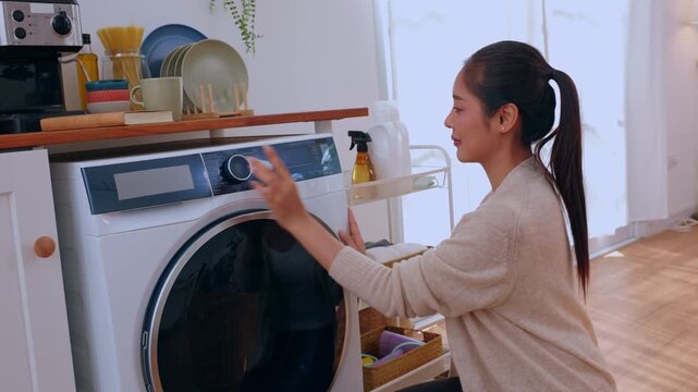 Woman washing machine laundry room cleaner spray bottle home cleaning appliance, laundry detergent basket, garment chore, calm domestic routine near kitchen shelf