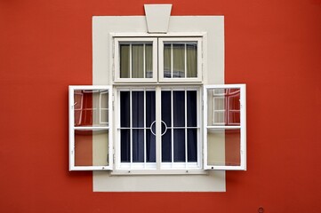 Obraz premium old style white wood window elevation closeup detail. steel security bars. open leaves, reflection on the glass. home concept. house facade detail. red stucco elevation with sandy texture. white trim 