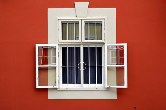 old style white wood window elevation closeup detail. steel security bars. open leaves, reflection on the glass. home concept. house facade detail. red stucco elevation with sandy texture. white trim 
