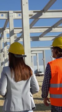Back View Tracking Shot of Engineers and Female Architect Walking Through Concrete Pillars Grid on Site. Teamwork, high-end infrastructure development, and occupational safety concept.
