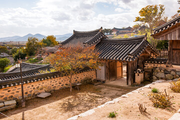 Fototapeta premium Exterior View of Traditional Korean Hanok Courtyard Featuring Wooden Buildings, Tiled Roofs, and Autumn Scenery Under a Cloudy Sky