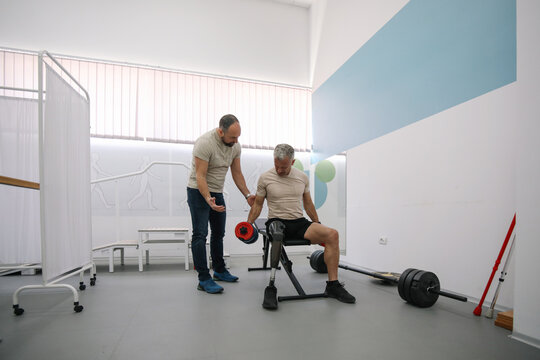 Veteran with prosthetic leg training with rehabilitation specialist in therapy gym