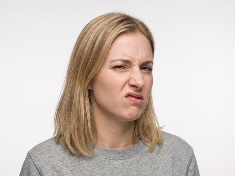 Close-up portrait of a young blonde woman showing a disgusted facial expression against a plain white background