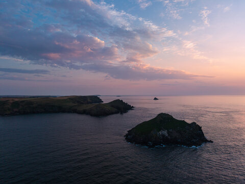Beautiful drone landscape image of Pentire Headland and The Rumps in Cornwall and surrounding countryside during colorful Summer sunset