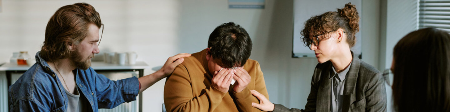 Header of young adults supporting distressed man during group therapy session, discussing emotional recovery and peer care. Ideal for mental health counseling, addiction support, wellness campaigns