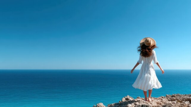 A woman in a flowing white dress stands at the edge of the sea, gazing at the vast ocean under a clear blue sky, representing freedom, peace, and connection to nature.