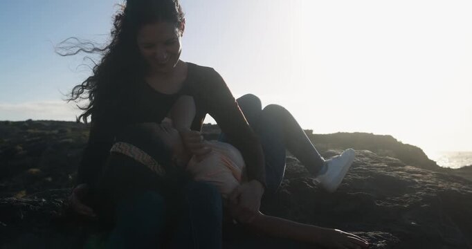 Happy latin mother having tender moment with female child on the beach during sunset time - Holiday, family lifestyle and bonding concept - UGC content