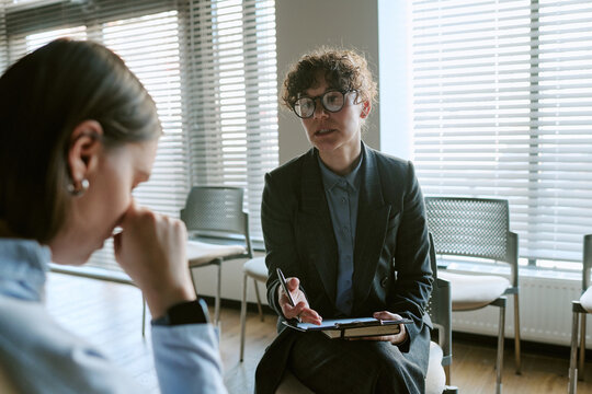 Female Caucasian therapist discussing mental problems with young woman, taking notes during session. Useful for psychology therapy sessions concept