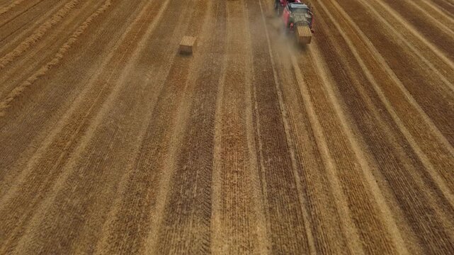 Aerial view of red square baler machinery baling straw on farmland after harvest
