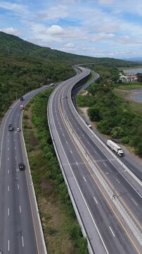 Vertical video Aerial view of highway running along river and green hills. Transportation, infrastructure, travel and logistics concept