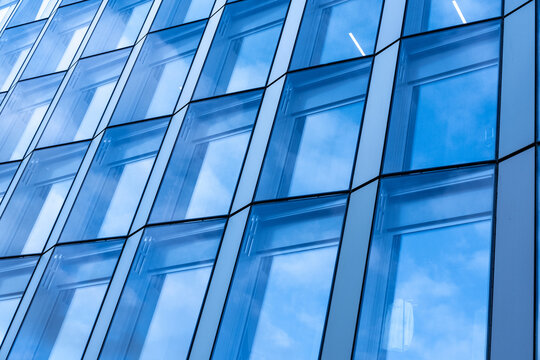 Across the angled surface, blue glass divides a building into windows, while reflection and geometry animate the facade and architecture of Oslo, Norway under daylight