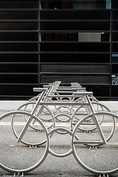 Across a paved area, empty bicycle racks repeat in metal rows, while parking geometry leads past an urban facade toward Oslo, Norway beneath horizontal shadows