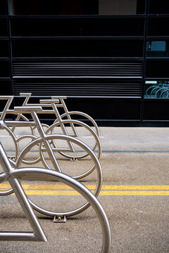 Within the vertical frame, bicycle racks follow a yellow line as cropped metal geometry defines empty parking beneath the facade of Oslo, Norway under daylight