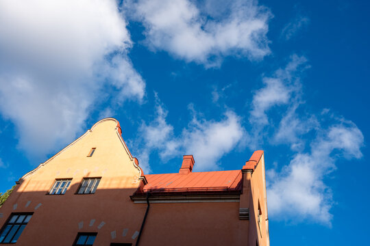 Drifting clouds open the view as a yellow building rises in perspective, its gable and facade shaping the architecture of Stockholm beneath a vivid sky in Sweden