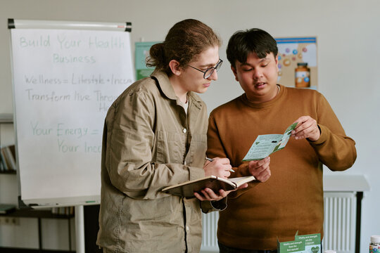 Young diverse colleagues reviewing supplement brochure and taking notes during wellness business training, supporting product education, sales onboarding, direct marketing use