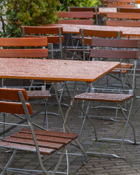 Rain covers outdoor tables and chairs in a street-side cafe during a wet day