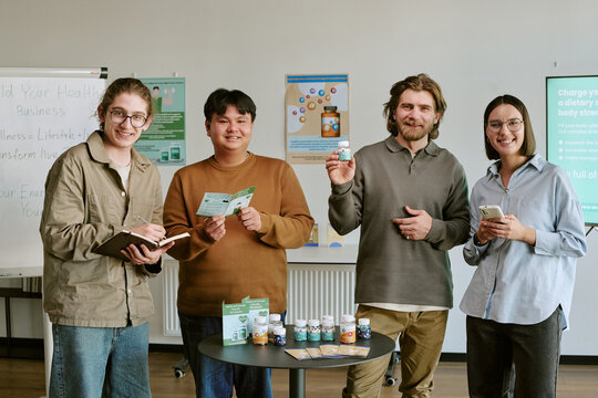 Portrait of diverse young adults presenting supplement products during business training, holding notes and phone. Useful for wellness sales education, product marketing, team onboarding