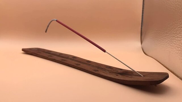 Burning sandalwood incense stick on wooden stand isolated on peach background
