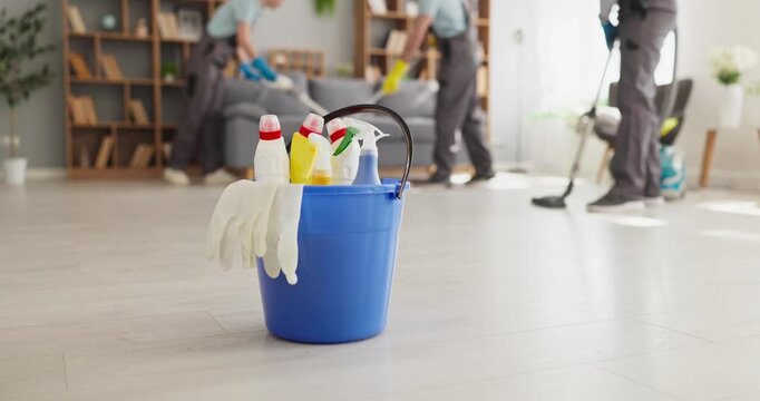 Cleaning cleaners team with bucket supplies gloves. Blue pail with spray bottles on floor as crew vacuum a bright home, showing housekeeping hygiene. Strong concept of cleaning service.