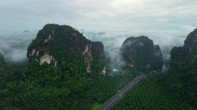 Aerial view of majestic limestone mountains surrounded by lush green tropical forest and morning mist in Krabi, Thailand.