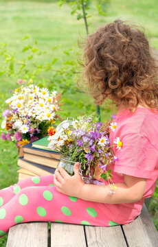 baby girl holding glass jar with meadow flowers and sitting on wooden bench outdoor, abstract natural background. Child in summer garden. relax, vacation concept. unrecognizable person, without a face