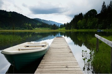 Obraz premium Serene lakeside dock with boat and mountain view. Tranquil outdoor scene for relaxation and nature lovers.