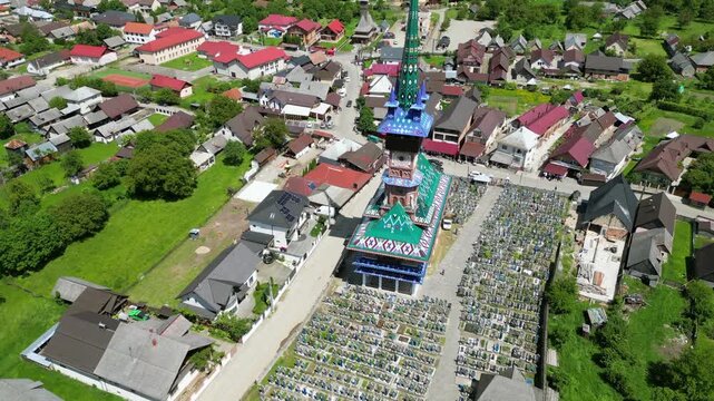 Aerial drone footage orbiting around the colorful church and painted wooden crosses of the Merry Cemetery - Cimitirul Vesel - in Sapanta