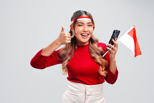 Beautiful young Indonesian woman is giving a thumbs up gesture while holding a cellphone.