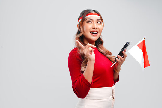 Joyful Indonesian woman holding a cellphone while pointing to the copy space behind her.