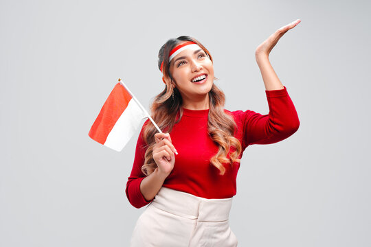 Happy young Asian woman is holding mini country flag and pointing to the copy space upwards.