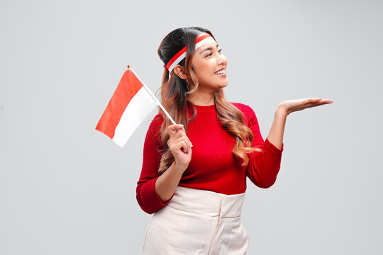 Pretty young Asian woman is holding mini country flag and presenting copy space beside her.
