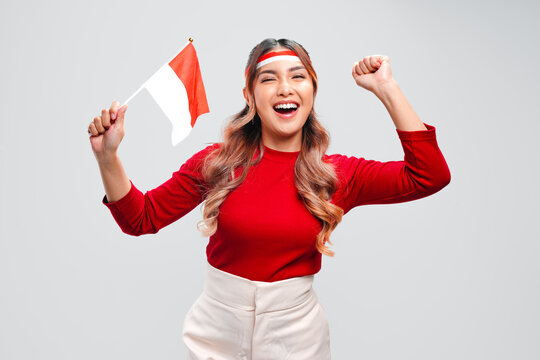 Excited Asian girl is raising fists doing celebration while holding mini country flag.