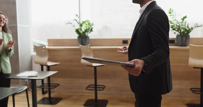 Speaker businessman gives presentation with tablet in office. Side view shows a leader gesturing during an office meeting with a concise strategy briefing. Coaching focus and leadership theme.