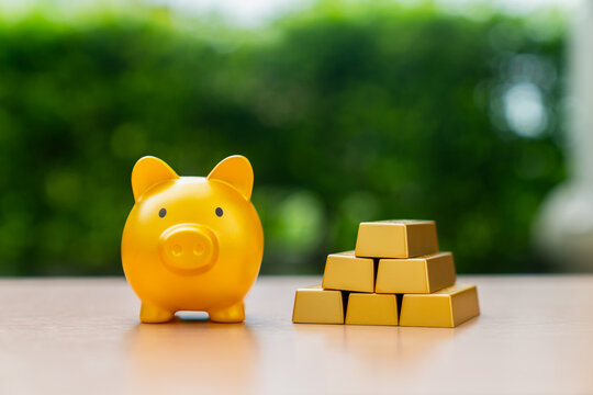 Yellow piggy bank and stack of shiny gold bars on table with green background.