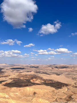 Aerial top view of a dry desert landscape with dramatic shadows from clouds over the Ramon Crater