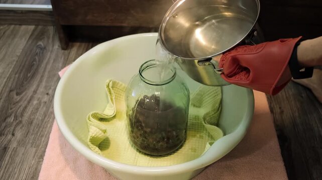 A man canning cherry compote using a manual seaming machine to seal a large glass jar with metal lid. Home canning, food preservation, traditional kitchen, winter storage preparations. A Can Seamer.