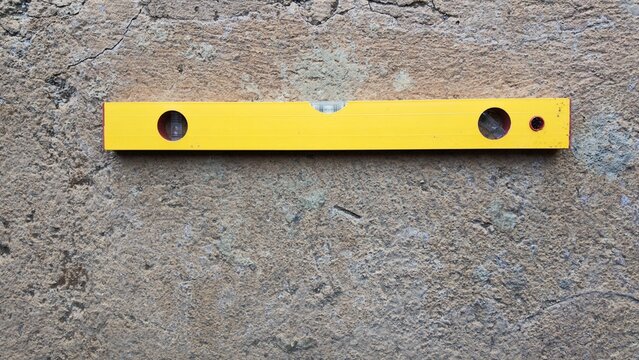 Top-down view of a yellow spirit level tool resting on a rough, textured concrete surface.