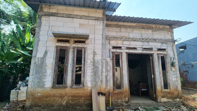 Front facade of an unfinished small house made of aerated concrete blocks, showing wooden doors and windows amidst construction debris.