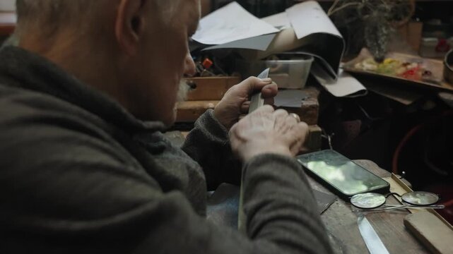Elderly craftsman working in his old workshop, carefully restoring collectible Japanese bladed weapons