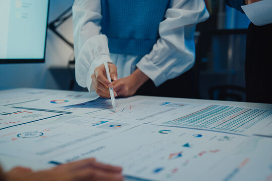 Close up Asia businesspeople meeting plan analysis statistics brainstorm and work with paperwork around table in office conference room at night. Business finance partners strategy investment success.